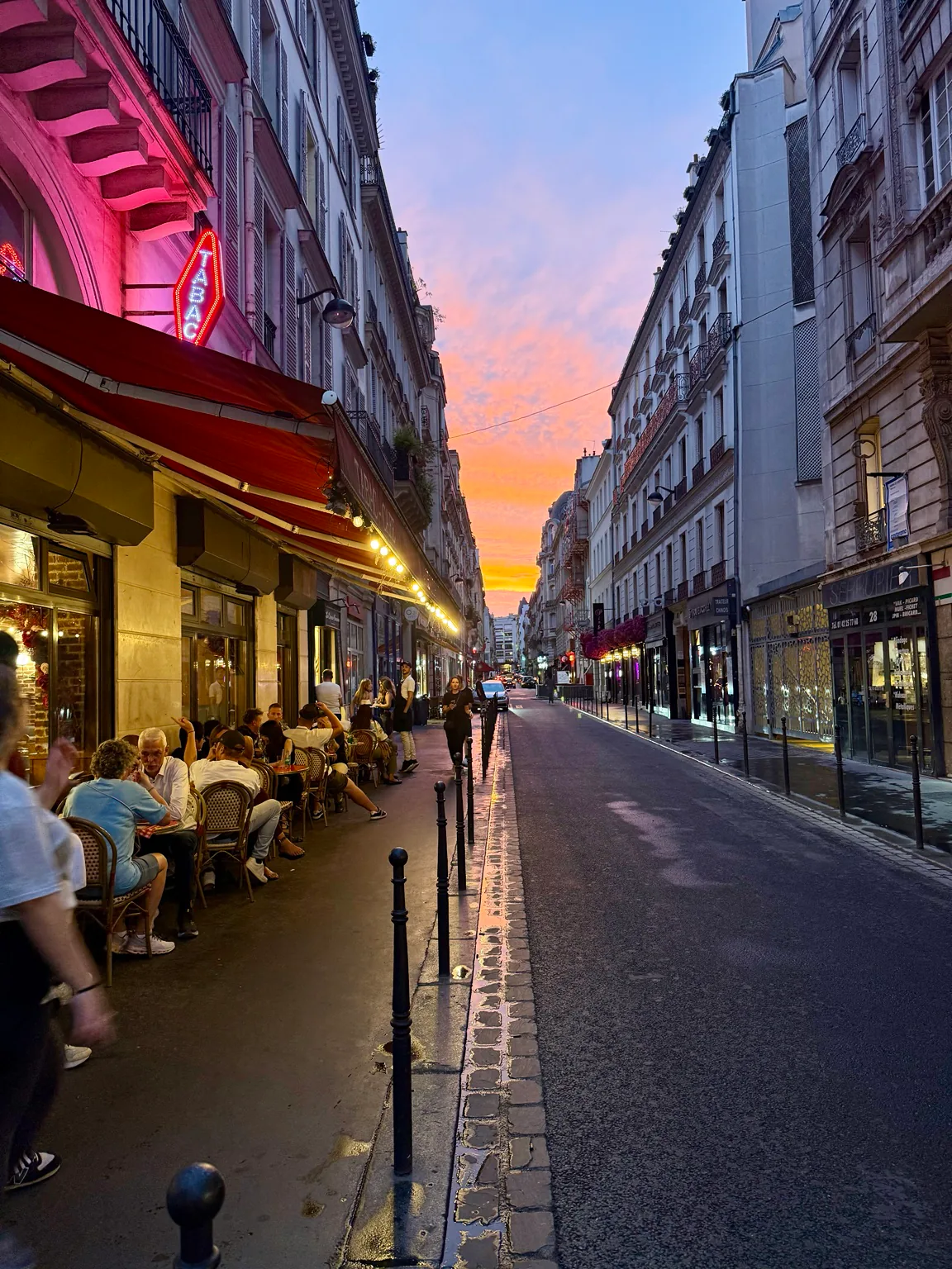 A café street glowing beneath a pink and gold sunset