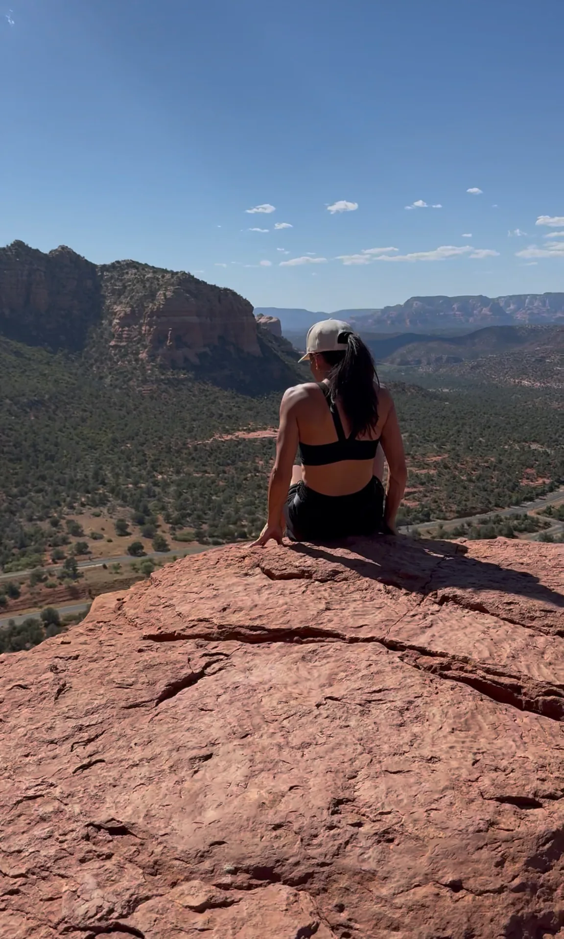 A woman pausing on red rock above a wide desert valley